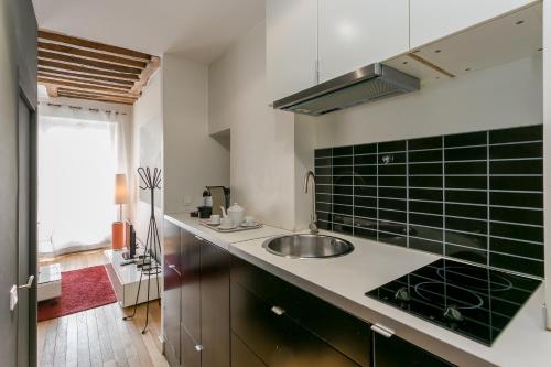 - une cuisine avec évier et carrelage vert sur le mur dans l'établissement Le Marais Place Sainte Catherine With AC, à Paris