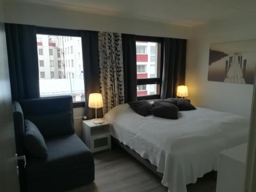 um quarto com uma cama, uma cadeira e 2 janelas em Apartment Oulu station em Oulu