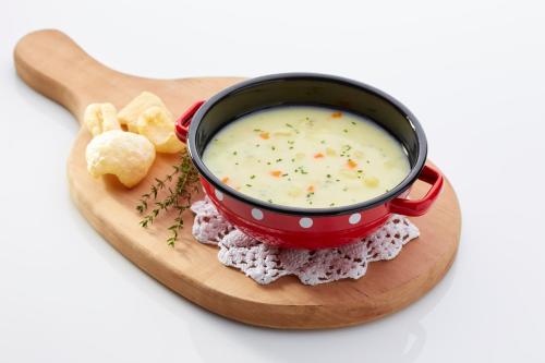 a bowl of soup in a red pot on a wooden board at Hotel Delalut in Ravne na Koroškem