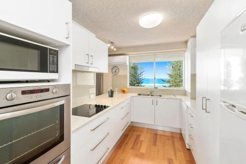 a kitchen with white cabinets and a large window at Solnamara Beachfront Apartments in Gold Coast