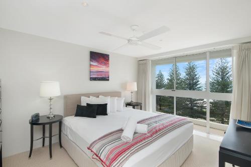 a white bedroom with a large bed and a window at Solnamara Beachfront Apartments in Gold Coast