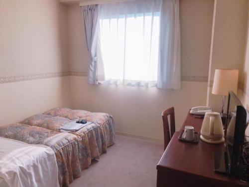 a hotel room with a bed and a desk and a window at Kagoshima Daiichi Hotel Kishaba in Kagoshima