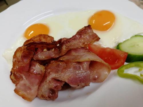 a plate of food with eggs and bacon and vegetables at Ipari Park Panzió in Szolnok