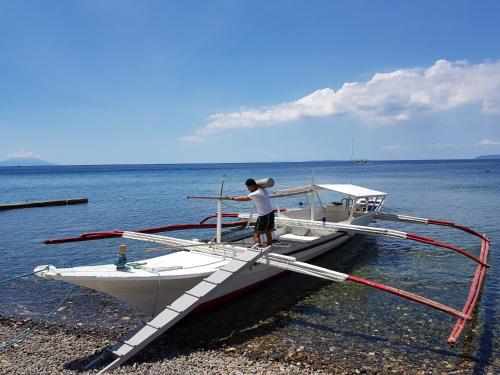 a man is standing on a boat on the shore at Blue Ribbon Dive Resort in Mabini
