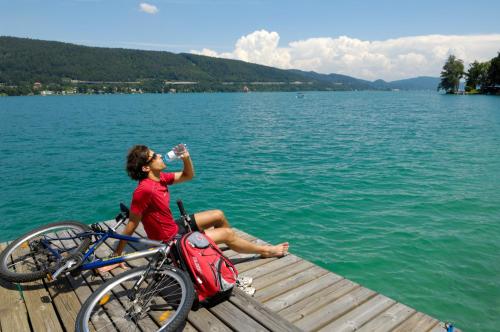 a woman sitting on a dock drinking from a water bottle at Dei Hotel Schönblick in Velden am Wörthersee