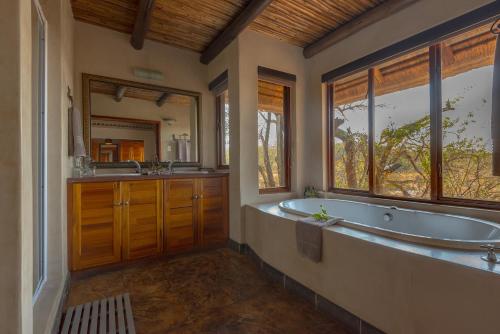 La salle de bains est pourvue d'une baignoire, de 2 lavabos et d'un miroir. dans l'établissement Waterbuck Game Lodge Thornybush Nature Reserve, à Domaine de chasse de Thornybush
