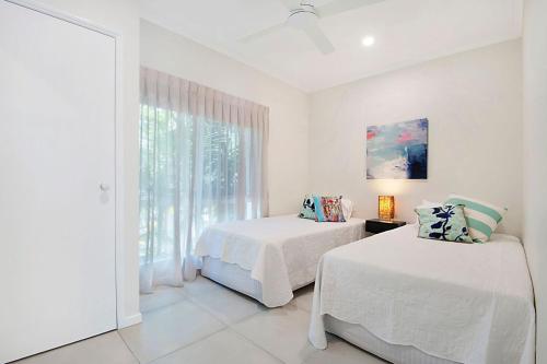 a white bedroom with two beds and a window at Durramboi Luxury Apartment in Noosaville