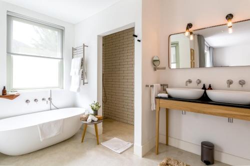 Maison Cabrière - Boutique Suites في فرانستشوك: حمام به مغسلتين وحوض استحمام ومرآة