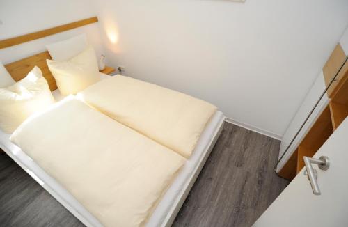 ノルダーナイにあるApartment mit Balkonの白いシーツと枕付きのベッドが備わる小さな客室です。
