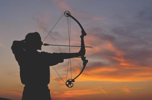 a man holding a bow and arrow at sunset at Anantara Qasr al Sarab Desert Resort in Jurayrah