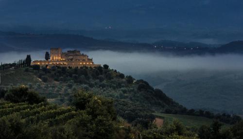 a castle on top of a hill in the fog at Castello di Velona Resort, Thermal SPA & Winery in Montalcino