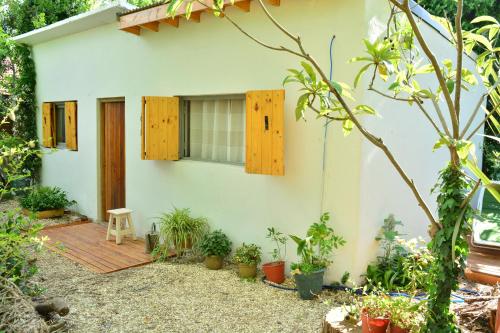 ein kleines weißes Haus mit Holzfenstern und Pflanzen in der Unterkunft La Casa de Huéspedes in Santa Teresita