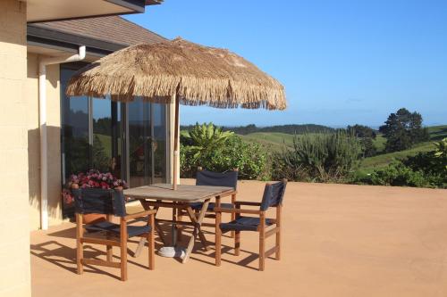 einen Holztisch und Stühle unter einem Strohschirm in der Unterkunft High Ridge House in Coopers Beach