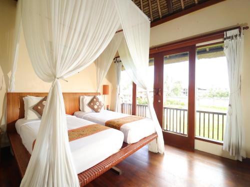 a bedroom with two beds with curtains and a balcony at Biyukukung Suite & Spa in Ubud