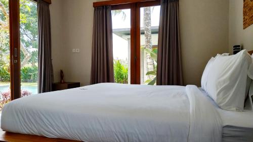 a bedroom with a white bed and a large window at Anggira Villa Ubud in Ubud