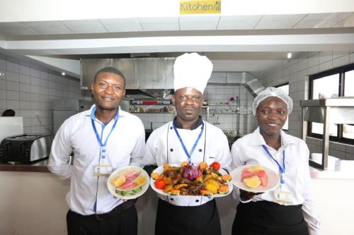 three chefs holding plates of food in a kitchen at Sheratton Regency Hotel in Mombasa