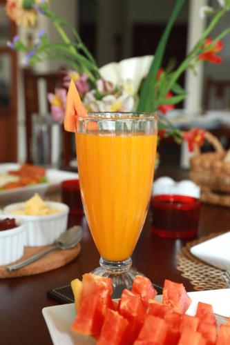 a glass of orange juice on a table with a plate of watermelon at The Wind Castle in Nuwara Eliya