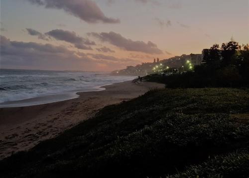 a beach at sunset with the ocean and lights at No 2 Heleza Blvd Sibaya, Oceandune, Umhlanga Durban in Umdloti