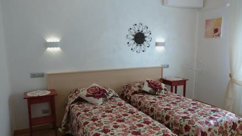 a room with two beds and two tables and a clock on the wall at Bed & Breakfast Delle Rose in Conegliano