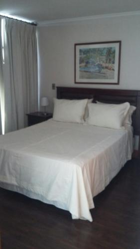 Una cama con sábanas blancas y almohadas en un dormitorio en Austral Rentahome Américo Vespucio Norte en Santiago