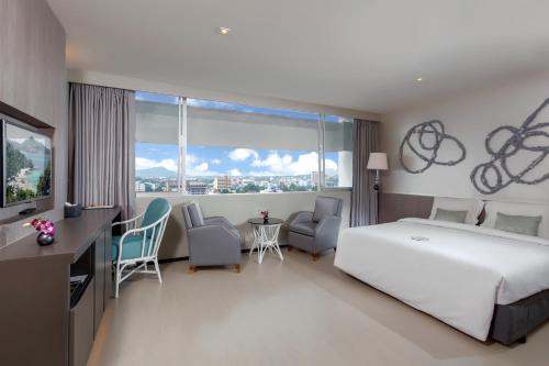 a hotel room with a bed and a large window at Pearl Hotel - SHA Plus in Phuket