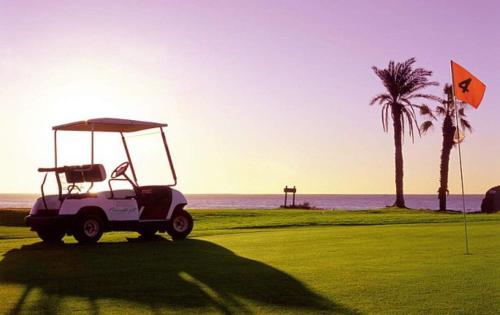 un carro de golf estacionado en un campo de golf cerca del océano en Moderno apartamento con vistas al mar, en Playa del Águila