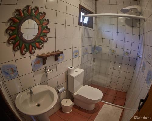 a bathroom with a toilet and a sink and a mirror at Pousada Watu Kerere in Praia do Rosa