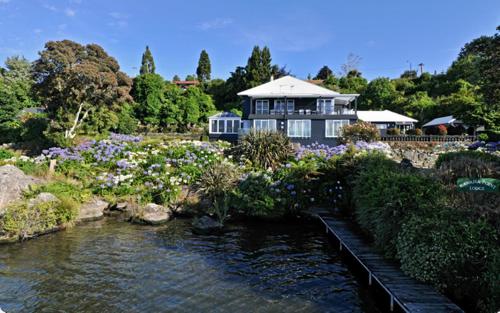 a house with a pond in a garden with flowers at Black Swan Lakeside Boutique Hotel in Rotorua
