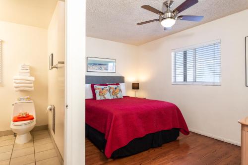 a bedroom with a bed with a red bedspread and a toilet at The Sea View Inn At The Beach in Manhattan Beach