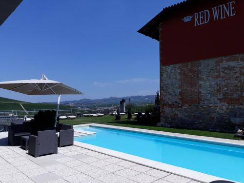 a swimming pool with an umbrella next to a building at Red Wine Camere in La Morra