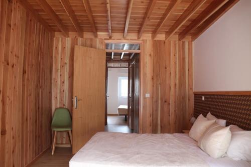 a bedroom with wooden walls and a bed with a green chair at Casa do Alpendre in Furnas