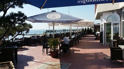 Ein Mann, der an einem Tisch unter einem blauen Schirm sitzt. in der Unterkunft Strandhotel in Wyk auf Föhr