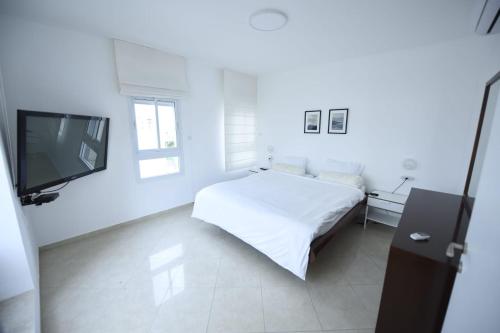 a white bedroom with a bed and a flat screen tv at Sea View Coral Suite in Eilat