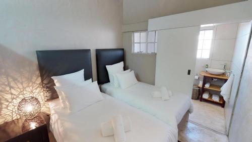 a bedroom with two beds with white sheets and a mirror at Swartberg Pass Cottages - Kobus Se Gat in Matjiesrivier