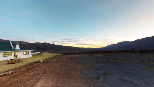 a house on a dirt road with mountains in the background at Swartberg Pass Cottages - Kobus Se Gat in Matjiesrivier