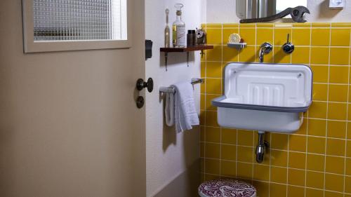 a bathroom with a sink and a yellow tile wall at The Originals City Hotel Artyster Clermont Ferrand in Clermont-Ferrand