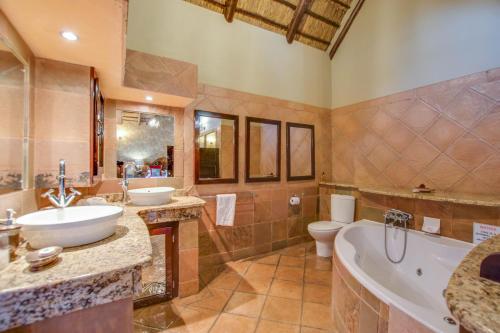 een badkamer met 2 wastafels, een bad en een toilet bij Kassaboera Lodge in Hartbeespoort