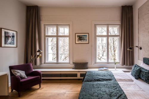 a bedroom with a bed and a chair and two windows at Hotel Oderberger in Berlin