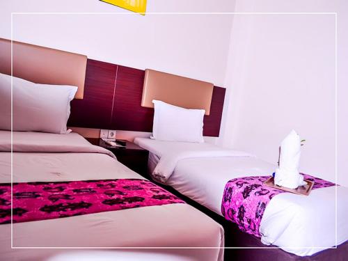 two beds in a hotel room with white and purple at Ayla City Hotel in Sorong