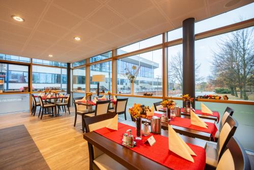 um restaurante com mesas e cadeiras e janelas grandes em Das Hotel an der Stadthalle - Rostock Hauptbahnhof em Rostock