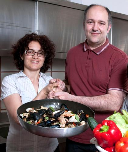 a man and woman standing in a kitchen with a pan of food at Hotel Amicizia in Rimini