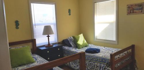a bedroom with two beds and a lamp and two windows at Blue Crab Cove in Oak Island