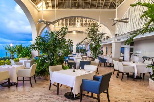 a restaurant with white tables and chairs and palm trees at Fairmont Royal Pavilion Barbados Resort in Saint James
