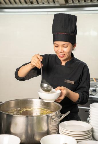 a woman in a kitchen stirring a bowl with a spoon at The Sailing Bay Beach Resort in Mui Ne