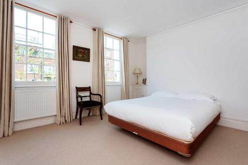 a white bedroom with a bed and a chair at Veeve - Sloane Square Hideaway in London