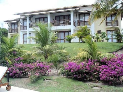 a building with palm trees and purple flowers in front of it at Condomínio Reserva Imbassai in Imbassai