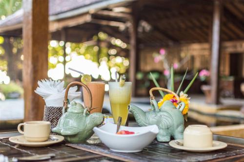 a table topped with cups and plates of food and drinks at Hotel Pondok Sari Beach & SPA Resort in Pemuteran