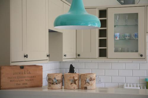 a kitchen with white cabinets and a blue light fixture at Owlers Retreat in Camber