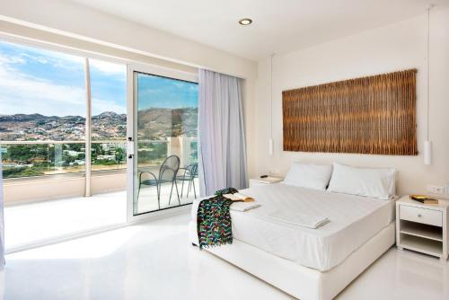 a white bedroom with a bed and a large window at Eva Mare Hotel & Suites - Adults only in Agia Pelagia