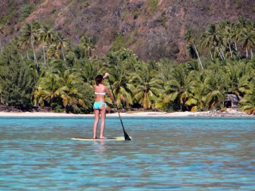 a woman in a bikini on a paddle board in the water at Robinson's Cove Villas in Papetoai